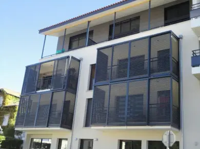 Cloisonnement de balcon avec des panneaux fixes de claustra aluminium et cloison coulissante à lames fixes ajourées.