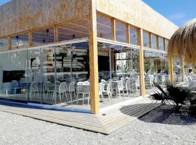 Coulissant Panoramique Glass Systems, solution de cloison en verre grand longueur pour fermer en angle une terrasse de restaurant en bord de mer.
