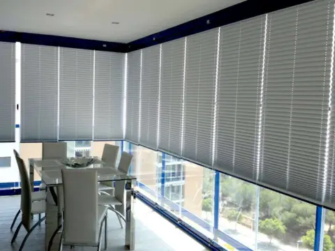 Terrasse couverte en étage fermée par un garde corps en verre combiné à un rideau de verre, protégé du soleil par des stores plissés et enrouleurs