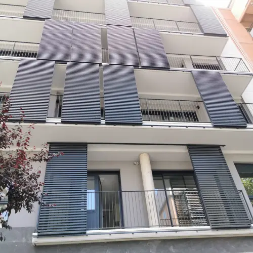 Vue générale d'un immeuble avec des cloisons coulissantes à lames fixes utilisées comme brise-soleil ou volet installé sur les balcons en applique.