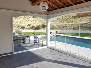 Cloison en verre extérieur Glass Systems installée en angle et en galandage pour fermer une terrasse donnant sur une piscine.