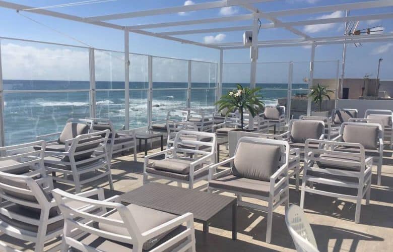 Paravent rétractable Glass Systems en pose sur une terrasse de restaurant en bord de mer pour se protéger du vent marin.