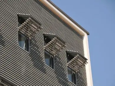 Exemple de volet papillon sur mesure en aluminium à lames fixes se confondant avec le bardage moderne de l'immeuble