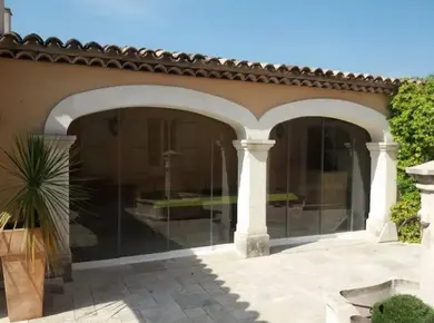 Vue extérieure d'un Coulissant Panoramique en Verre Glass Systems qui ferme une terrasse avec des arches.