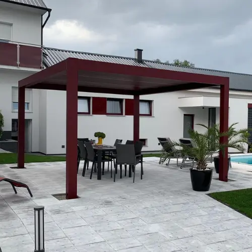 Pergola bioclimatique autoportée en aluminium rouge bordeaux couvrant le mobilier de jardin proche d'une piscine.